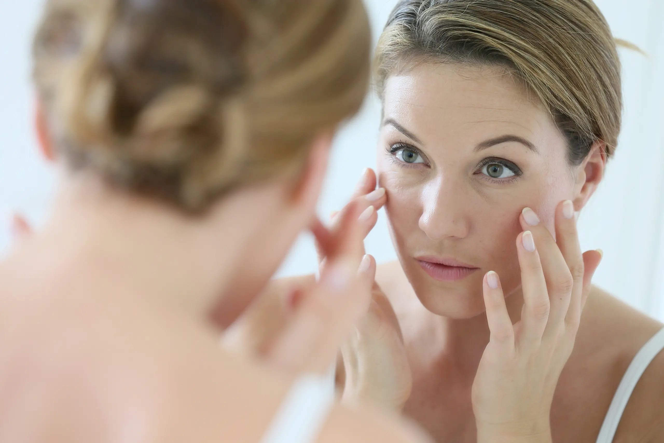 Jeune femme observant ses traits marqués au niveau des yeux illustrant les besoin classiques de médecine esthétique de la peau